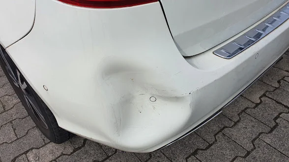 Deutlich eingedrückte weiße Stoßfängerecke neben einem Parksensor